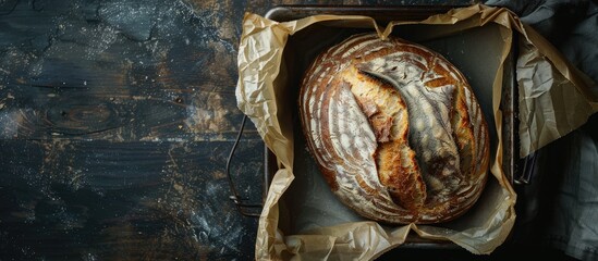 Poster - A rustic sourdough bread loaf placed in a square metal baking pan with parchment paper, set on a dark wooden surface, captured in a horizontal photo with ample copy space image.