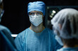 © Seventyfour - Portrait of male surgeon wearing scrubs and protective gear with medical team in operating room lit by blue light copy space