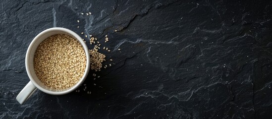 Aufkleber - Copy space image of organic sesame in a white cup on a black slate background.