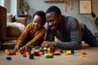 © Татьяна Евдокимова - Father and his young son are lying on the floor, smiling and playing with building blocks together