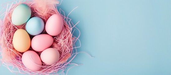 Colorful Easter eggs arranged in a pink nest on a soft pastel blue background in a close-up copy space image.