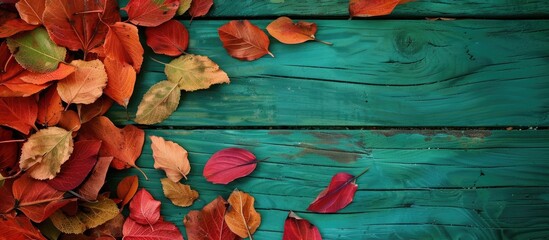 Poster - Fall-colored dried leaves piled up on a green wooden surface with a blank area for text or images, creating a natural and seasonal copy space image.