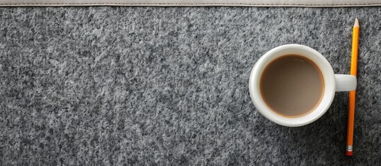 Poster - Bird's-eye view of a white coffee mug and pencil on a gray felt desk pad with a clear space for images. image with copy space