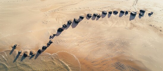 Aufkleber - Aerial view of a meandering line of black stones on a sandy beach, providing ample copy space for an image.