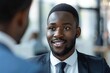 © Yuliia - young African American businessman interviewing a male candidate in an office setting.