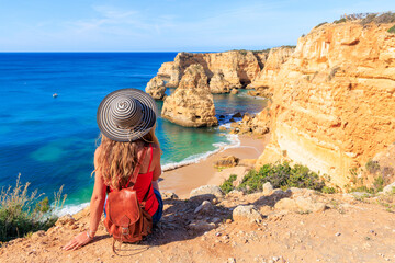 Wall Mural - Female tourist sitting on cliff enjoying awe sea and rocks panoramic view