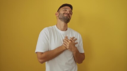 Poster - Young hispanic man wearing white t-shirt standing gratefully with hand on chest, feeling healthily content and smiling over isolated yellow background