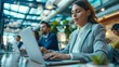 © venusvi - A businesswoman typing on a laptop during a meeting, with colleagues in the background discussing