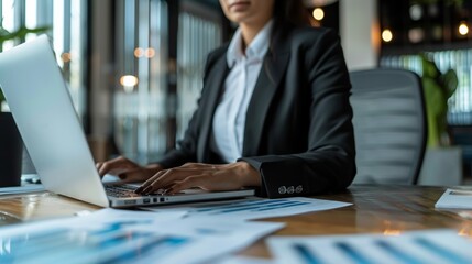 Poster - A business professional in a modern office, focused on their laptop with documents spread out on the desk
