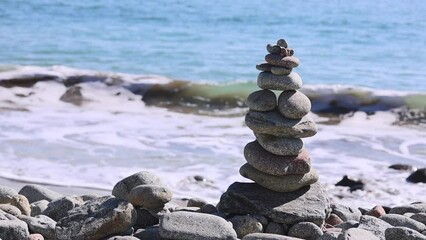 Wall Mural - A stone tower found on a beach with many small, round pebbles. Mongdol Beach with waves comeing in, Slow motion