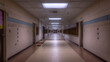 © Nasreen - A quiet, vacant corridor in a school building, stretching far ahead with neatly arranged lockers and doors to classrooms, lit by overhead lighting.