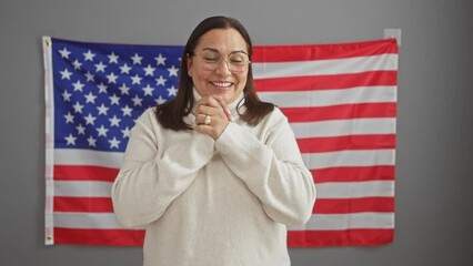 Sticker - Joyful middle age hispanic woman in glasses stands victorious at office, winning smile ablaze, celebrating achievement and united states flag behind her.