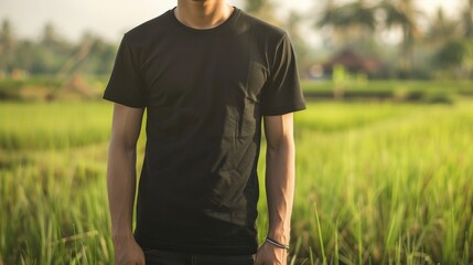 A man wearing a black t-shirt stands in a grassy field