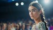 © liliyabatyrova - A beautiful young woman with a braid in her hair looks directly at the camera with a confident expression. She is standing on a runway with a blurred background of people and stage lights