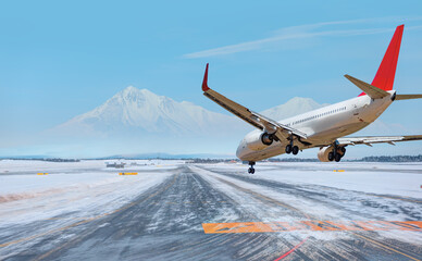 Wall Mural - White Passenger plane landing to runway snowy mountains in the background - Snow-covered airport