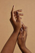 © Seventyfour - Vertical close up on elegant hands with nude manicure of African American woman. Monochrome nail design in dark brown shades against beige background