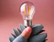 © PRANA - hand holding a light bulb on pink background