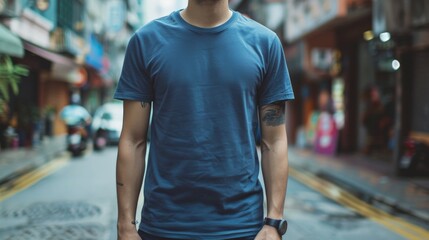 A man wearing a blank teal t-shirt walks down a city street