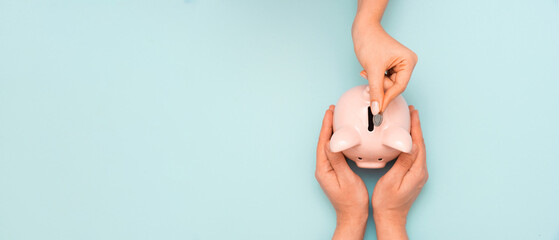 Wall Mural - Hand putting coin to piggy bank, top view