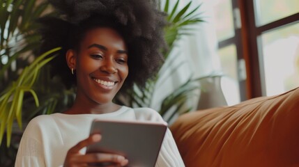 Wall Mural - A woman smiles while holding a digital tablet looking at the screen with interest and satisfaction