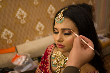 The makeup artist preparing Indian bride in traditional attire, adorned with intricate jewelry