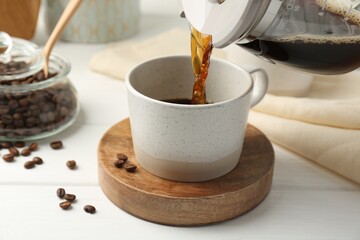 Canvas Print - Pouring coffee into cup at white wooden table, closeup