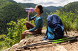 © Home-stock - Woman hiker hydrating her body, holding bottle with natural mineral water, sitting on rocks with beautiful mountains view