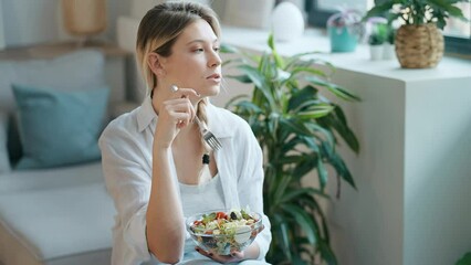 Wall Mural - Video of smiling woman eating healthy salad while sitting on the kitchen at home.