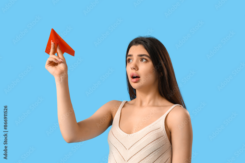 Upset young woman with paper plane on blue background