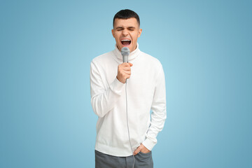 Wall Mural - Young man singing with microphone on blue background