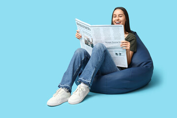 Wall Mural - Beautiful young woman in beanbag chair with newspaper on blue background