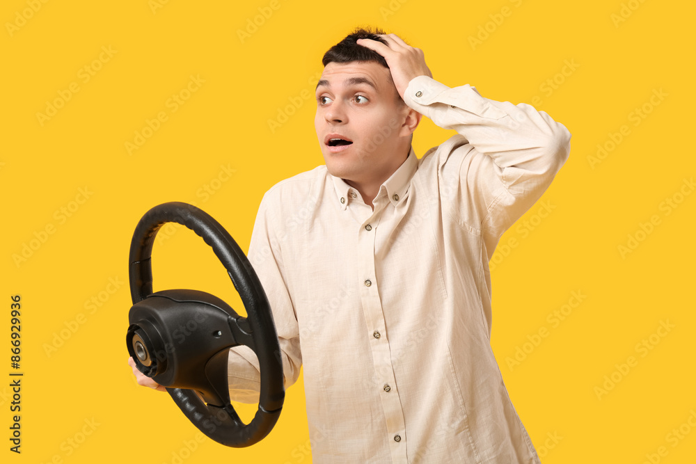 Shocked young man with steering wheel on yellow background