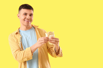Wall Mural - Handsome young man with tasty doner kebab on yellow background