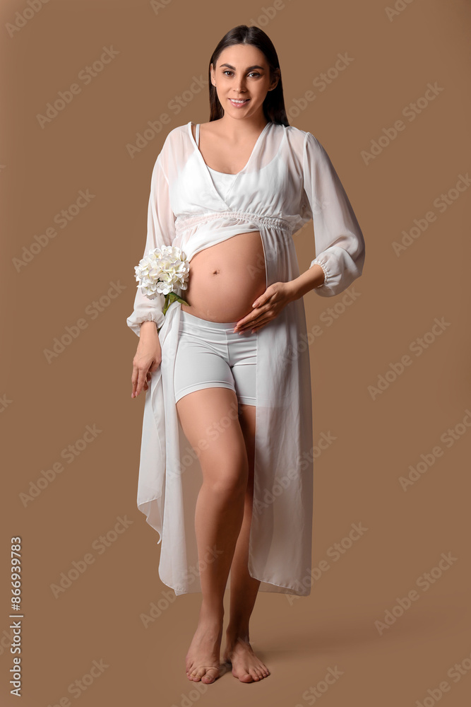 Young pregnant woman with hydrangea flower on brown background