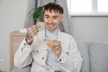 Poster - Young tattooed man with bottle of CBD oil sitting on sofa at home