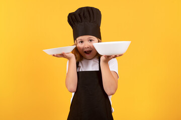 Wall Mural - Little cook with cooking plate. Chef kid boy making healthy food. Portrait of little child in chef hat isolated on studio background. Child chef. Cooking process.