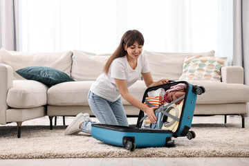 Canvas Print - Woman packing suitcase for trip on floor indoors