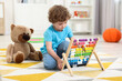 © New Africa - Cute little boy playing with wooden abacus on floor in kindergarten