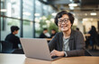 © Minimal Blue - A smiling woman wearing glasses, working on her laptop in a modern office setting with colleagues in the background