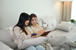 © Prathankarnpap - Happy Asian lesbian couple relaxing on couch and reading book together. LGBTQ people lifestyle concept