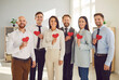 © Studio Romantic - Portrait of a diverse group of happy businesspeople stands in the office, holding red hearts and smiling. Valentine day or a volunteer initiative, showcasing love, togetherness, unity.