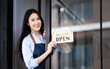 © NAMPIX - Startup successful small business owner beauty girl stand with open sign board in coffee shop restaurant.