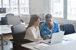 © insta_photos - Two busy middle aged professional business leaders talking working together on computer in office. Executive bank manager consulting client using laptop at meeting. Candid photo, view through glass.