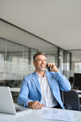 Busy happy middle aged business man talking on mobile phone working on laptop sitting in office. Mature professional businessman executive manager making call on cellphone using computer. Vertical.