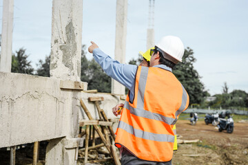 Wall Mural - Two male construction workers, including an Asian engineer, meticulously review structural plans and design concrete columns and beams for a new residential build.