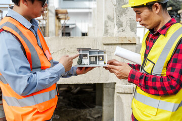 Wall Mural - Two male construction workers, including an Asian engineer, meticulously review structural plans and design concrete columns and beams for a new residential build.