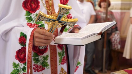 Wall Mural - The priest reads a prayer, holding a cross and a book in his hands.