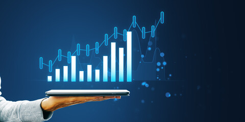 Poster - A person's hand holding a tablet displaying a holographic growth chart on a dark blue background, symbolizing business analytics