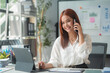 © amnaj - Asian businesswoman talking on phone and taking notes in office