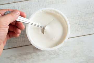 Wall Mural - A top down view of a hand dipping a spoon into a package of dairy-free sour cream.